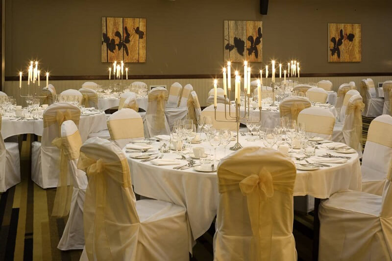 Wedding Breakfast room dressed with white table cloth and matchign white chair covers and lit up candles in the middle of the tables