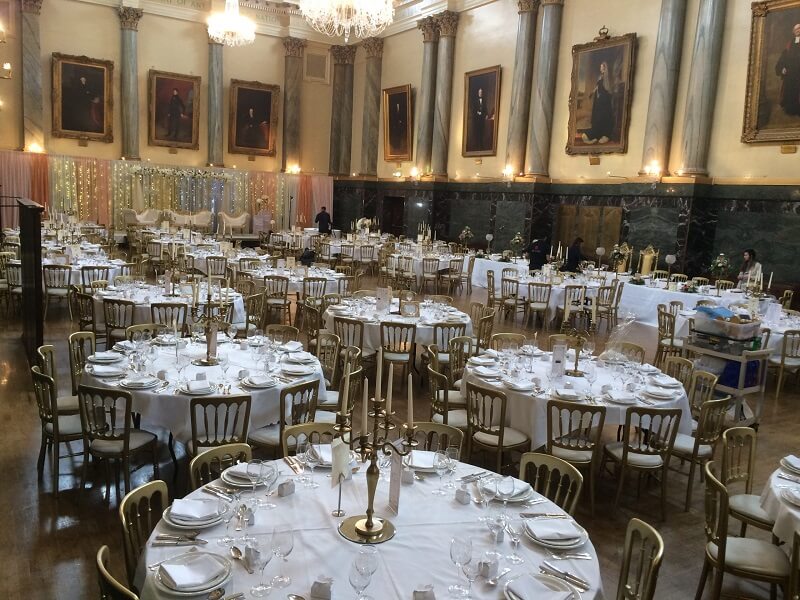 Aerial photo of a large wedding room with lit up chandelliers and period painting on the wall. 