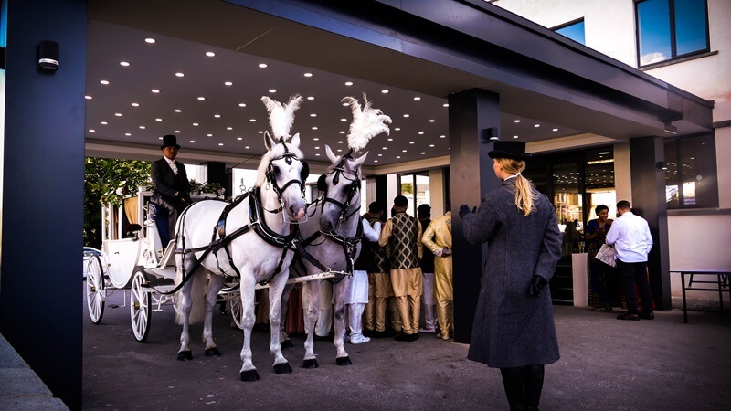Two white horses with their horseman pulling a white carriage stopped in front of HQ banqueting in Bradford