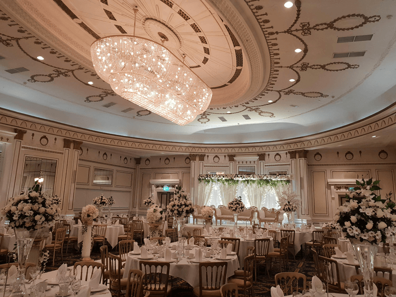 Reception Room at the Midland Hotel in Bradford with large sparkle light on the roof. Room is decorated with large white flowers in the middle of the tables