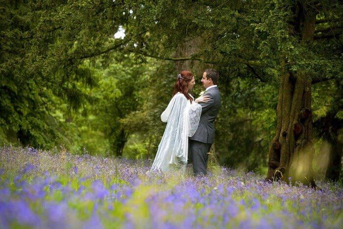 Bride and Groom facing and holding each others in a field of purple lavender and green trees in the background