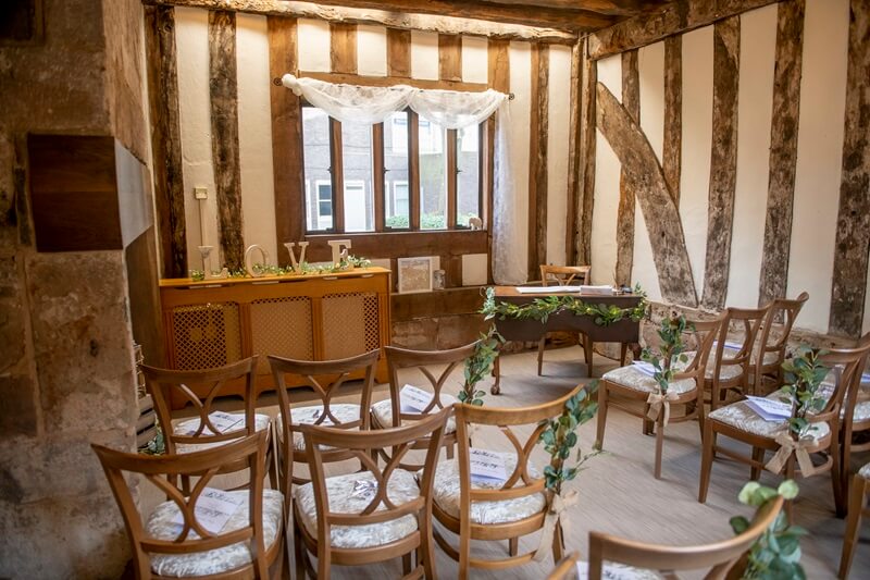 Ceremony room with wooden chaires decorated with green foliage and a LOVE sign by the registrar table.