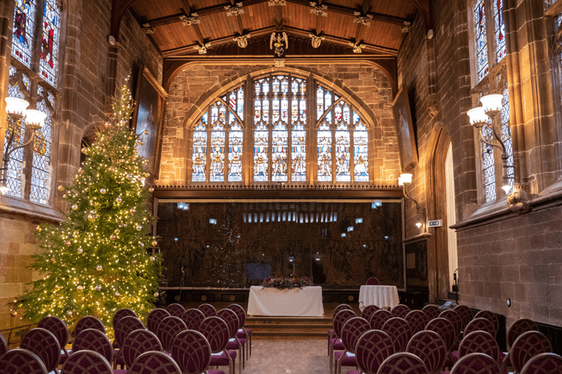 Ceremony room with high ceiling, vaulted windows with stained glass window. Lit up Christmas tree by the registrar's table