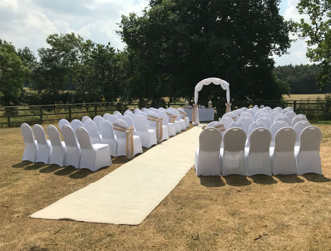 Outdoor Ceremony with white arch by the Registrar's table and chairs covered with White chair cover and ivory sashes