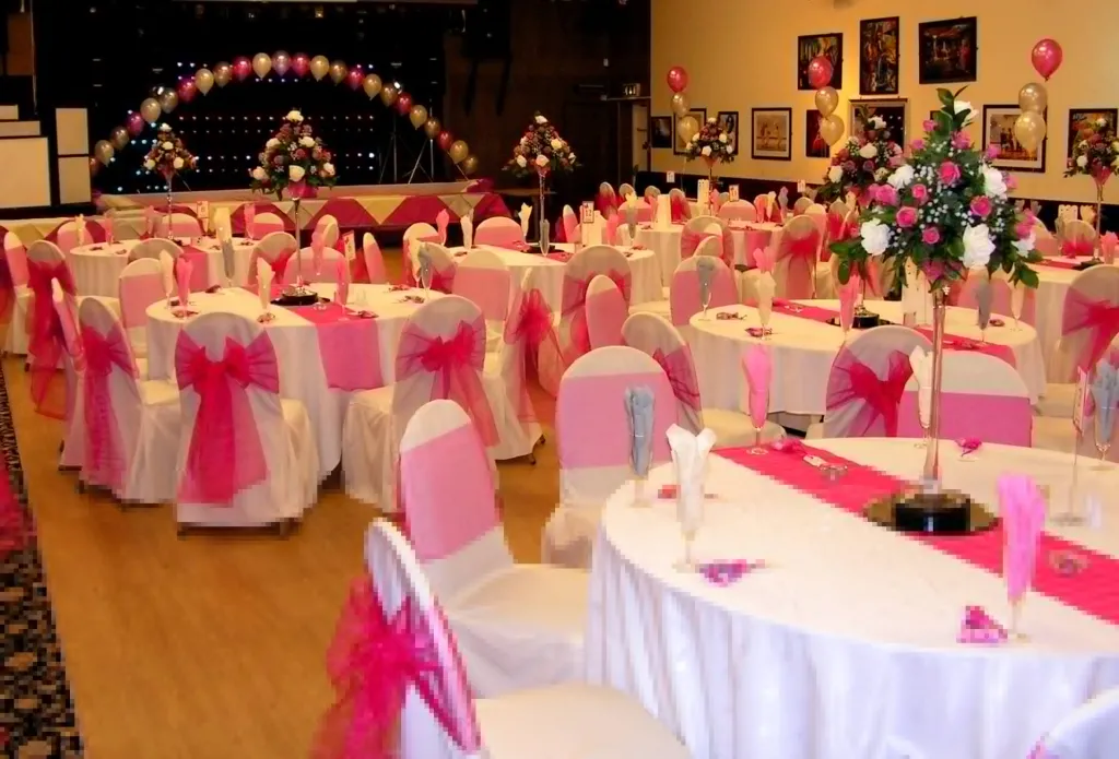 Reception Room at Massey Ferguson Social Club decorated in a Pink and White theme. White chair covers with pink sashes and centre table flowers in pink and white roses.