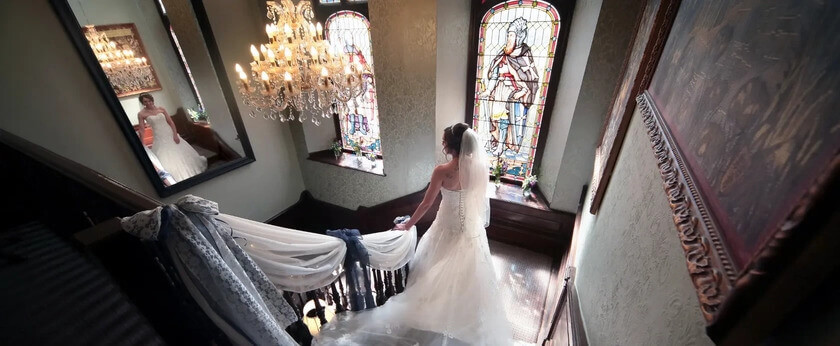 Bride wearing a white wedding dress walking down a large staircase. 