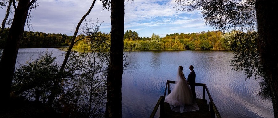 Bride and Groom holding hands on a wooden pond by the edge of a lac at twilight