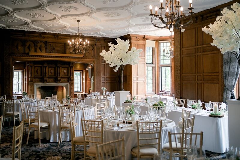 Wedding Reception Room with wooden walls, ceiling with art decor, lit up chandeleirs and round table with white table cloths