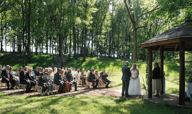 Outdoor wedding ceremony with guests seated on chairs looking at the Bride and Groom exchanging vows