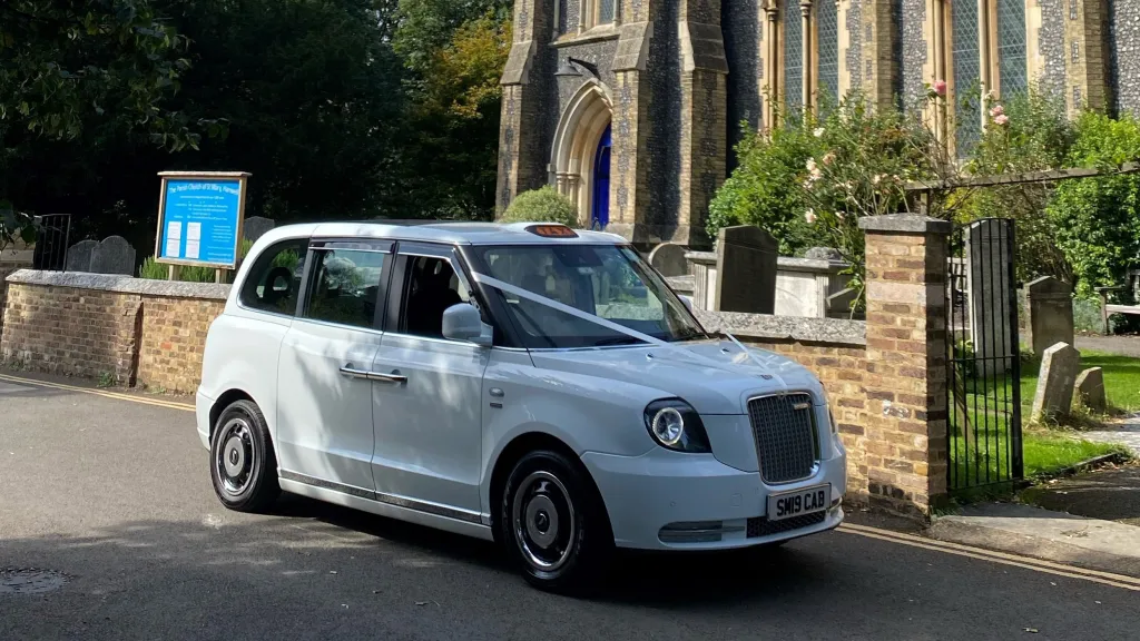 White Electric Taxi London Taxicab dressed with white ribbons parked in front of a church