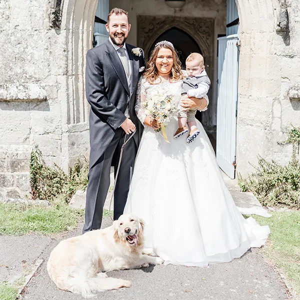 Family portrait in front of a church with Bride, Groom their baby child and dog