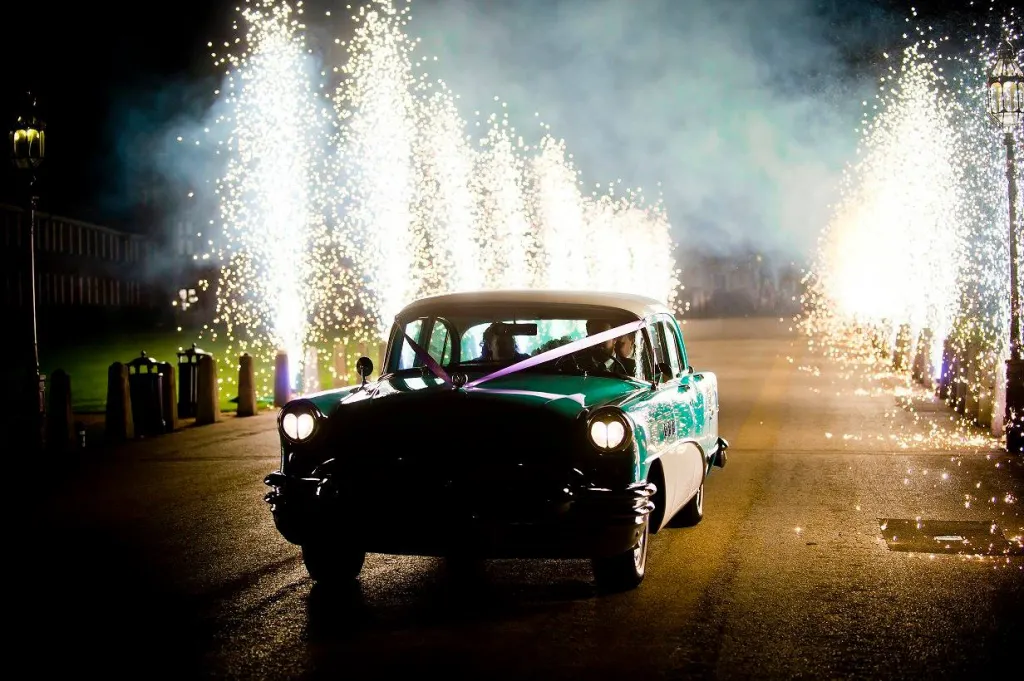 Classic Car driven at night with flares on both side of the road. 