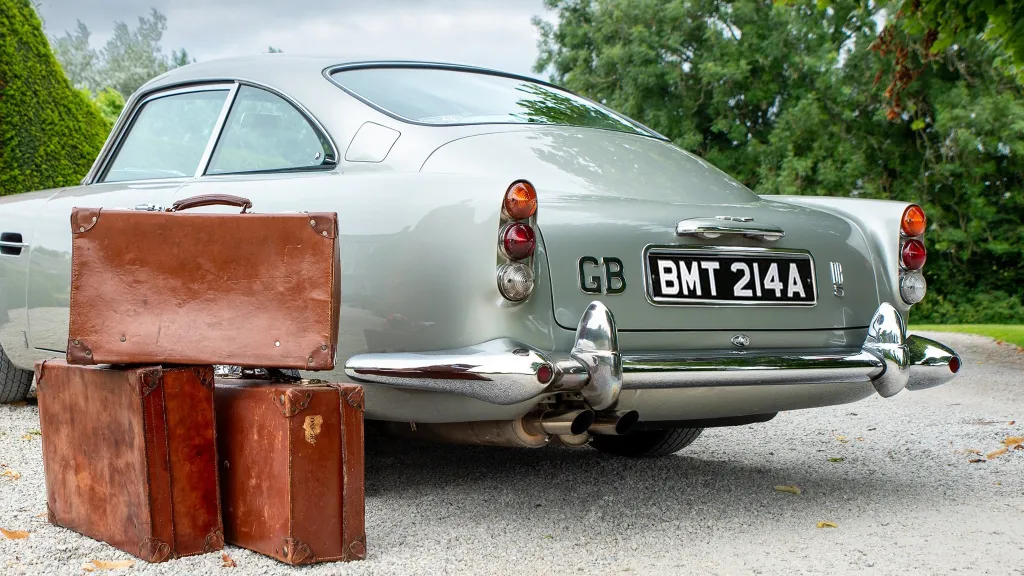 Classic Aston Martin rear view with three old fashion suitcases piled up next to the vehicle