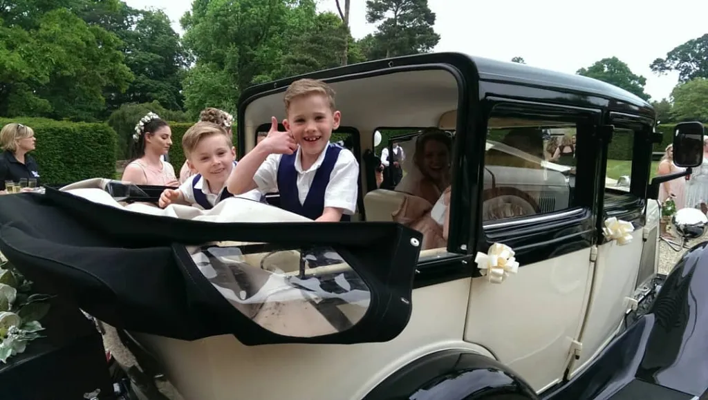 Happy children at a wedding waving from the rear seat of a convertible vintage car