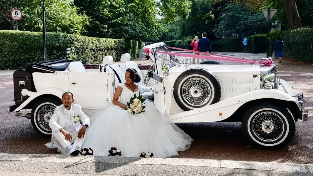 a white fully-convertible Beauford with roof open and Bride and Groom seating on the side of the vehicle.