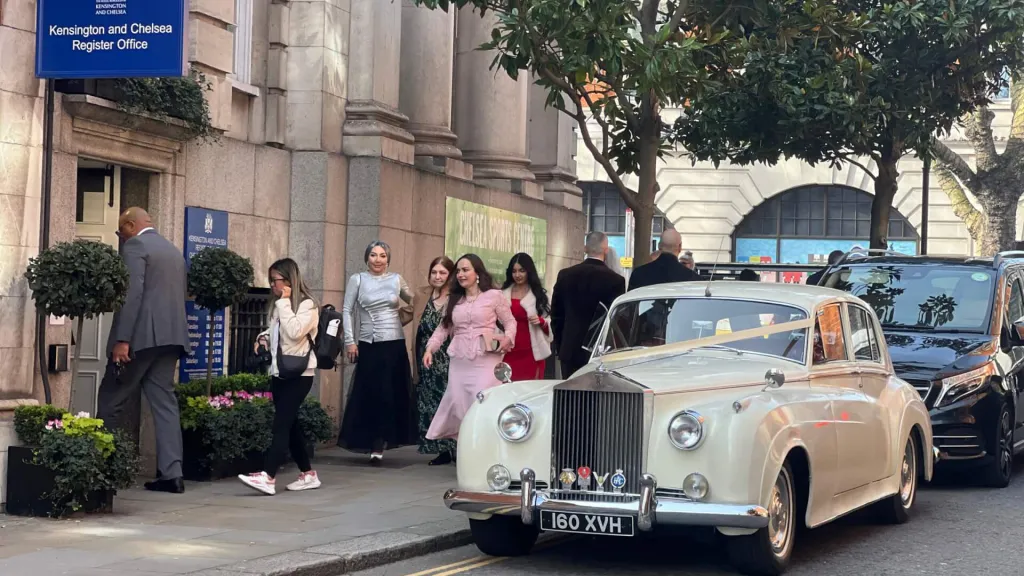 Rolls-Royce Silver Cloud wedding car outsode Chelsea Town Hall with wedding guests in the background