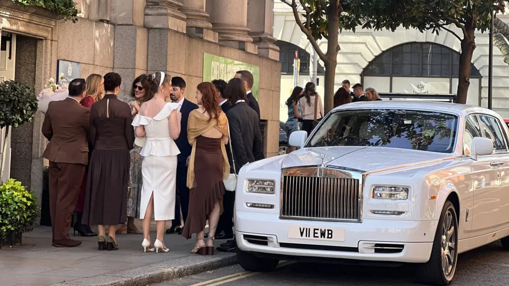 Modern White Rolls-Royce Phantom Series 2 parked outside Chelsea Town Hall with wedding guests in the background