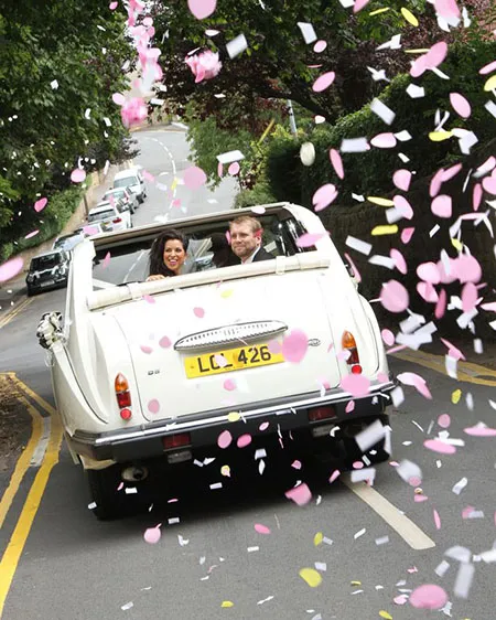 Classic Convertible Wedding Car with Confetti and Brinde and Groom enjoy their first journey together