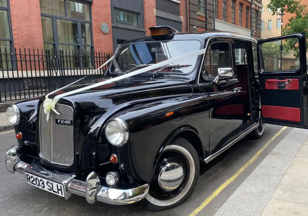 Classic black cab wedding car decorated with simple white ribbons and bow