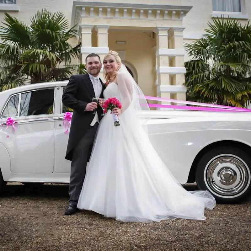 White classic Rolls-Royce wedding car with pink ribbons and bows matching the bridal bouquet