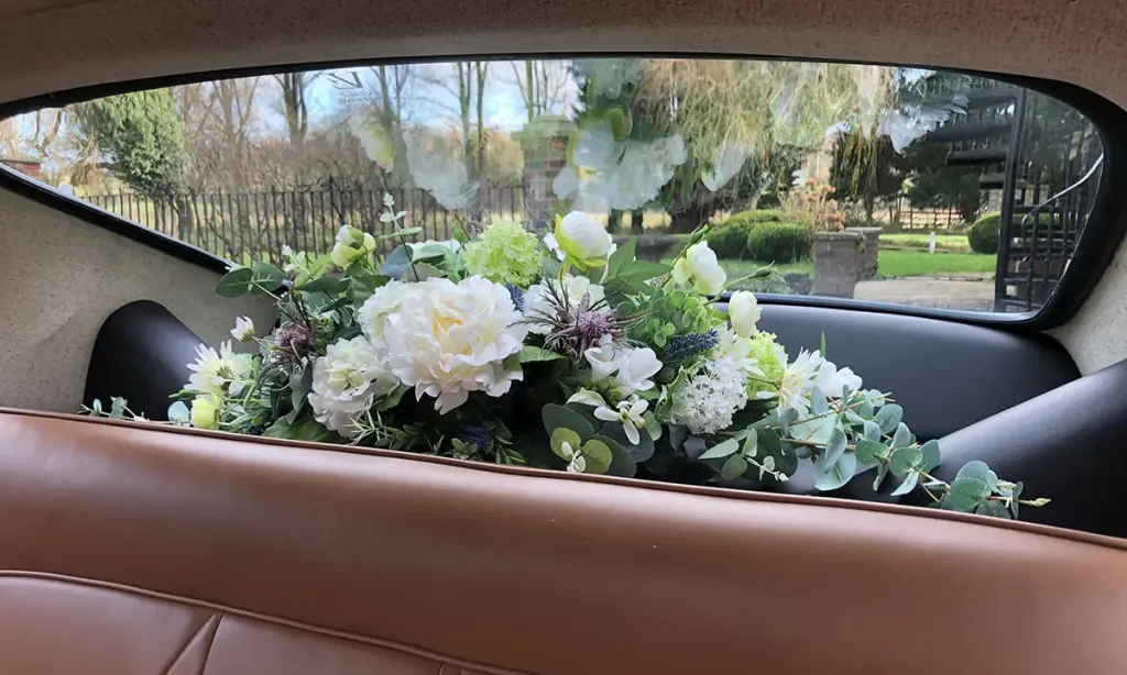 White and green faux wedding flowers arranged on the rear parcel shelf of a classic car