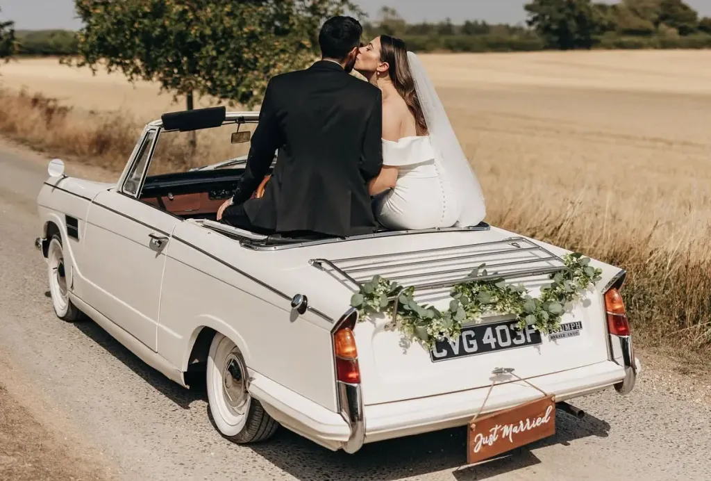 Happy wedding couple beside a decorated classic convertible wedding car