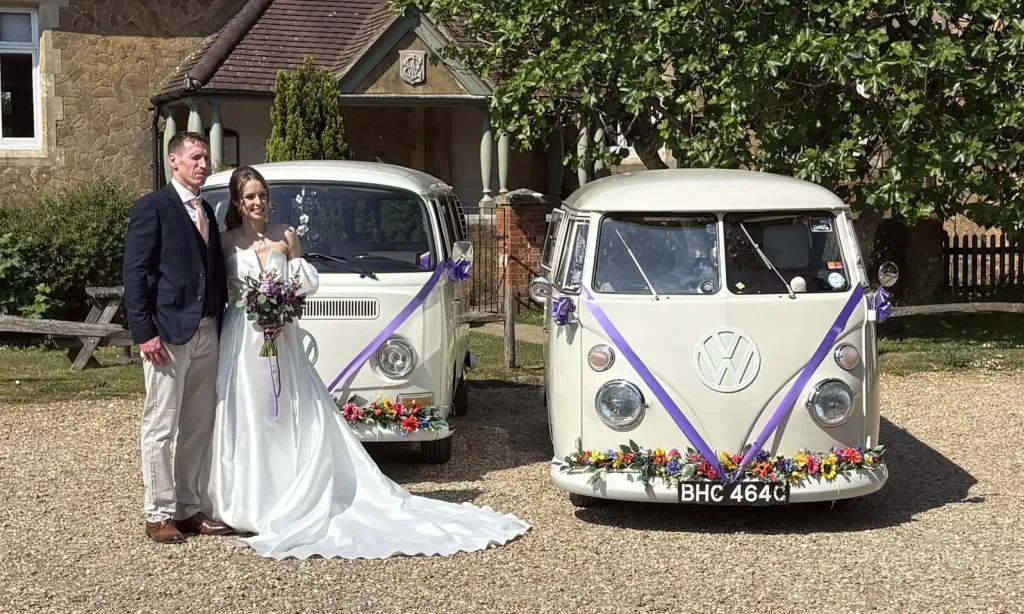 Matching ivory VW Campervans decorated with flower garlands and purple wedding ribbons