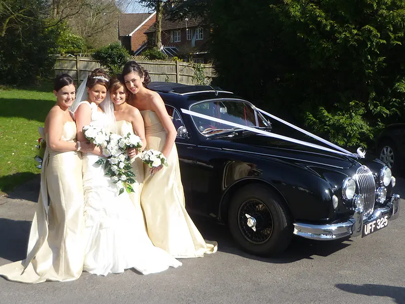 Bride and three bridesmaids in gold dresses beside the black Jaguar MK2 used in the TV series Endeavour
