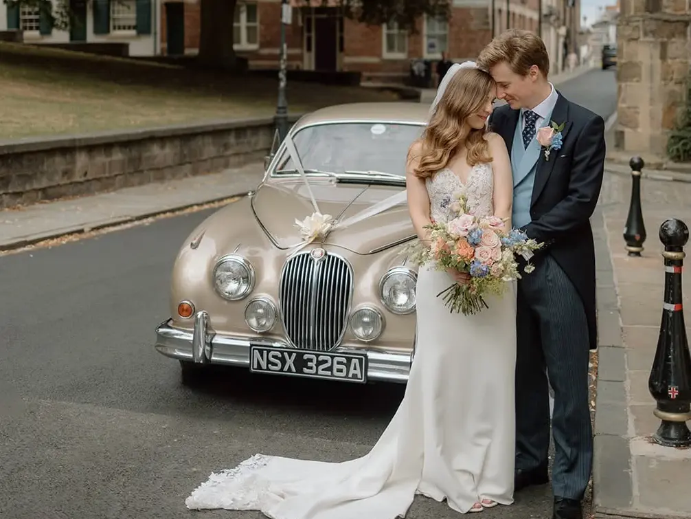 Bride and groom in front of an Opalescent Golden Sand Jaguar MK2 on a town street
