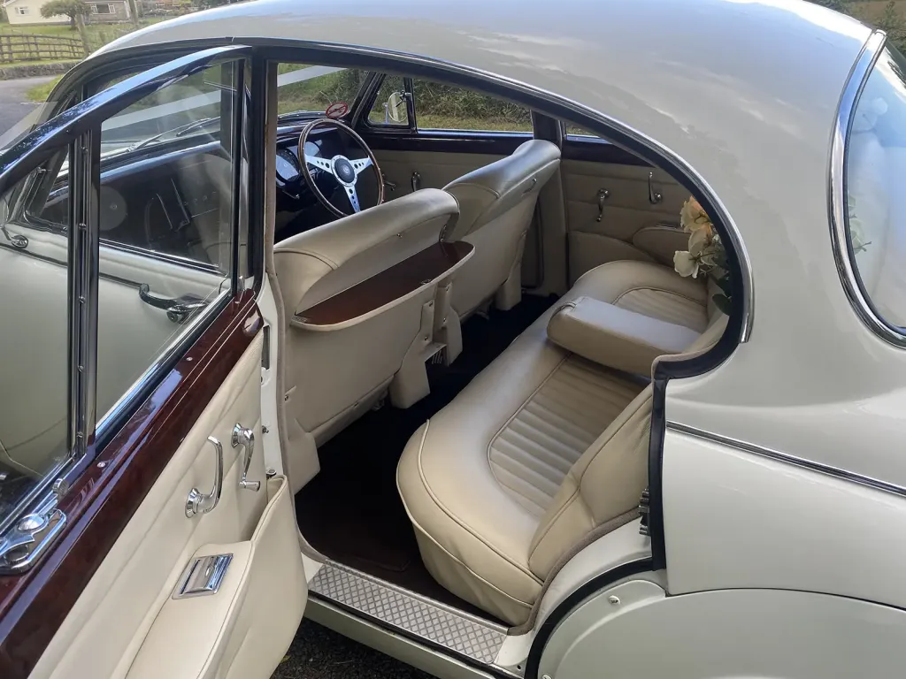 Cream leather rear bench seat, walnut door trims and fold-down picnic tables inside a classic Jaguar MK2