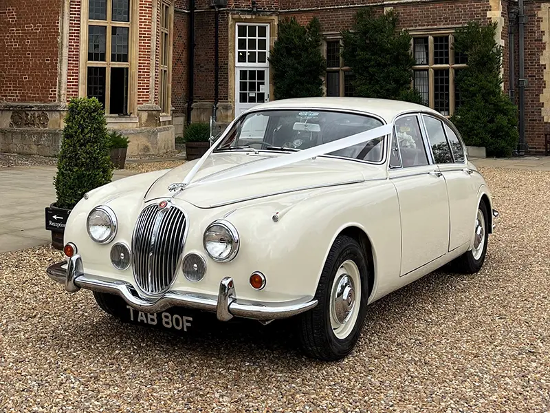 Old English White Jaguar MK2 with white wedding ribbons outside a Tudor red-brick manor house