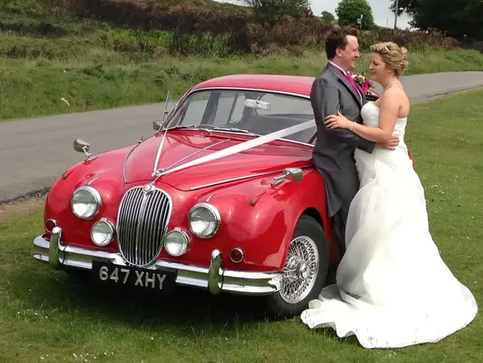 Bride and groom beside a red Jaguar MK2 3.8 with wire wheels on a country road