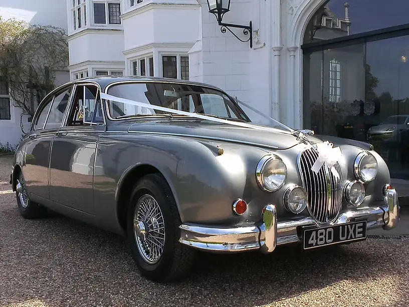 Silver grey Jaguar MK2 with wire wheels and white ribbons outside a white country house