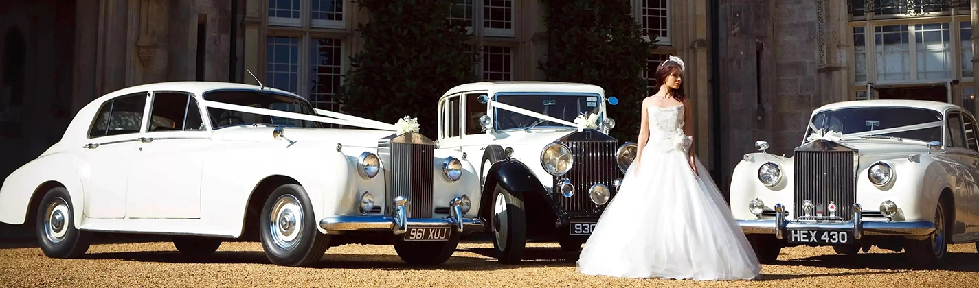 Wedding scene with a bride standing by three ribbon-decorated Rolls-Royce cars parked outside a popular wedding venue in Barnham.