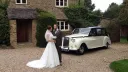 Bride wearing a long white dress standing by her husband with a Classic Black & Ivory Austin Princess Limousine in the background