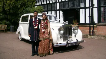 asian couple having photos next to their white vintage rolls-royce