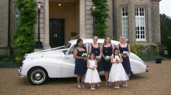 bridesmaids and flower girls in front of the car.