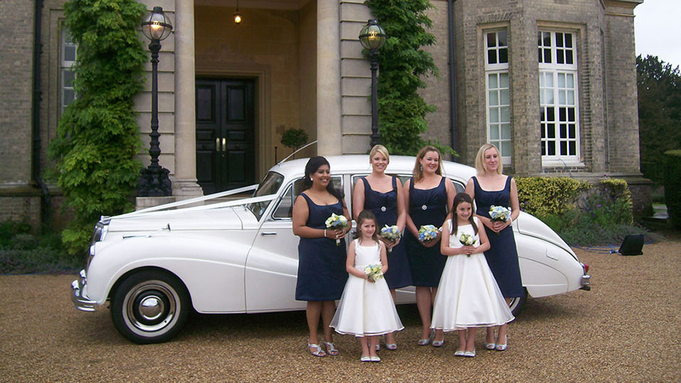 bridesmaids and flower girls in front of the car.