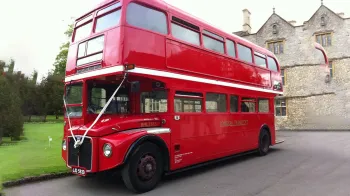 Red doubler decker London Routemaster Bus decorated with white ribbons across front parked ourside a wedding vue