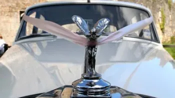 Spirit of ecstasy on top of the Chrome bumper on a Rolls-Royce Silver Cloud with light dusty pink ribbons