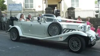 Vintage Beauford Convertible parked in street of cardiff with Bride and Groom inside and pale pink ribbons