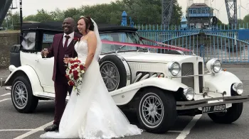 Bride and Groom holding each others in front of a Beauford convertible