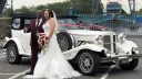 Bride and Groom holding each others in front of a Beauford convertible