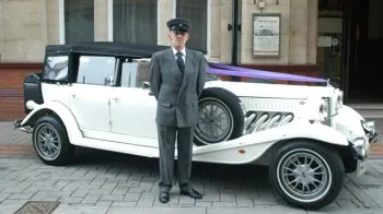 Chauffeur in a grey suit and hat standing in front of Ivory Beauford
