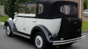 Rear view of white vintage-style regent wedding car with black soft top roof closed, thin rear chrome bumper and  black picnic trunk at the back of the vehicle