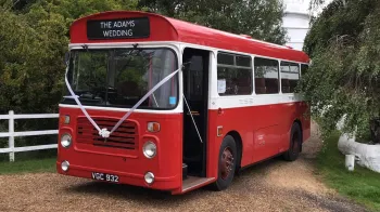 Left side view of White and Red classic single decker with front passenger door open and decorated with white ribbons and bow at the front