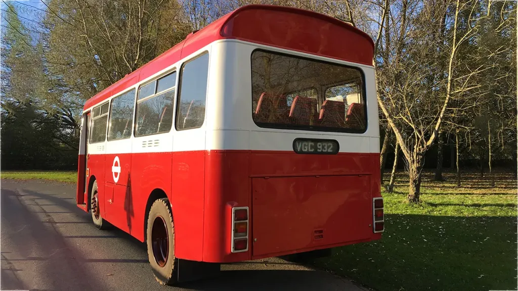 rear view of a white and red single decker bus parked on the side of the road in a park
