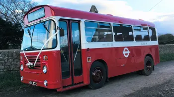 Left side view of a white and red classic Single decker bus with front doors closed