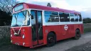 Left side view of a white and red classic Single decker bus with front doors closed
