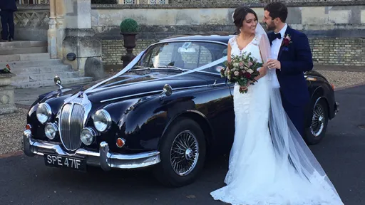Groom holding bride in his arms with Dark blue Daimler 250 V8 in the background